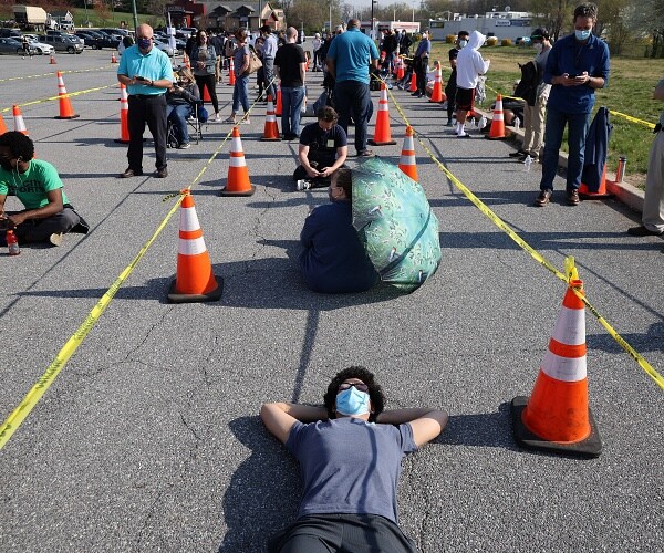 man lays on ground while waiting in line for vaccine
