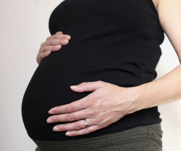 a pregnant woman, in a black maternity top, cradles her baby bump