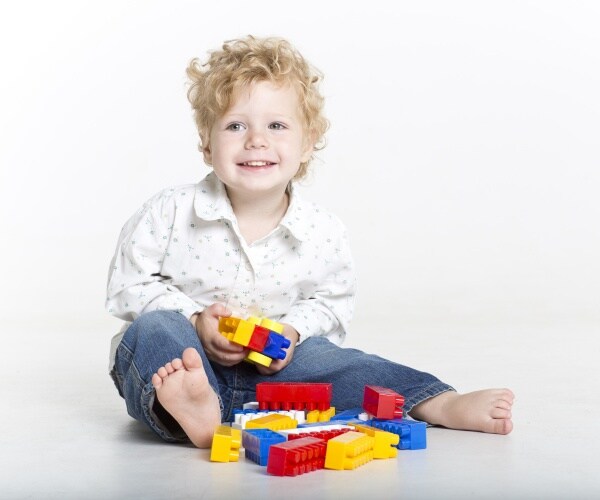 little boy wearing a button down shirt and jeans plays with legos