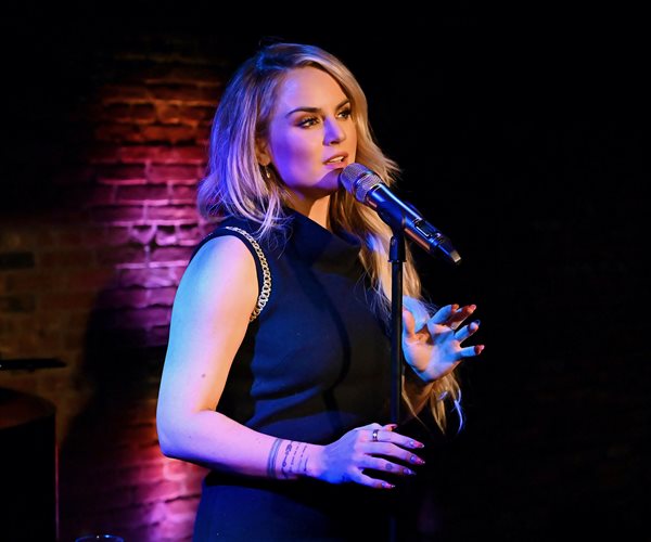 jojo wearing a dark sleeveless dress sings into a microphone