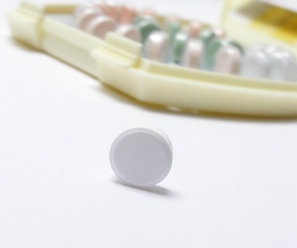 one pill on counter in foreground, with a pack of contraceptive pills behind