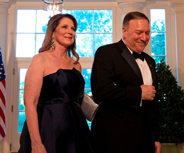 susan and mike pompeo, dressed in black tie, walk past a flag