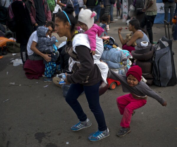 A Honduran migrant carries a little girl and drags another at a shelter in Tijuana, Mexico,