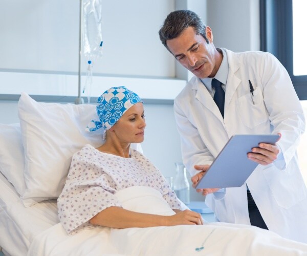 young woman in bed in hospital with cancer talking to her doctor