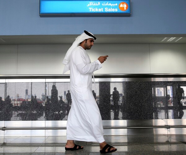 a man in a traditional white tunic looks at his phone at an airport in uae