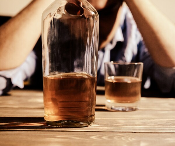 a bottle and glass of alcohol on a table in front of a man with his hands on his head