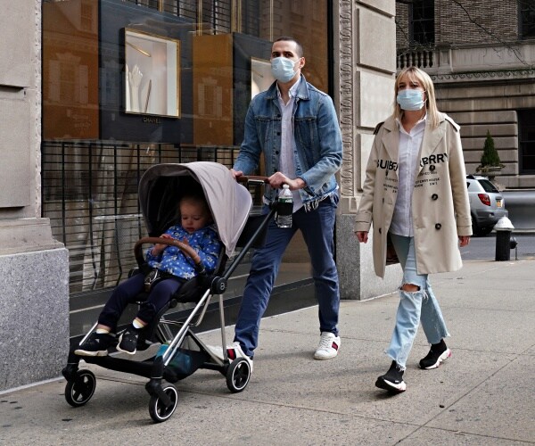 man in a mask and denim jacket pushes a stroller and woman wearing a a mask walks beside him