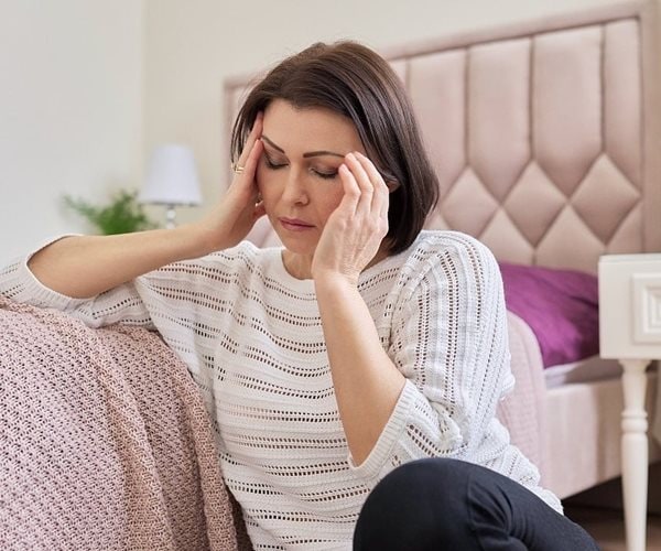 woman sitting on floor holding head in pain