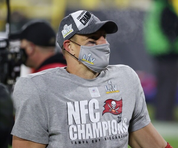 gronkowski in a gray t shirt and face mask and a baseball cap
