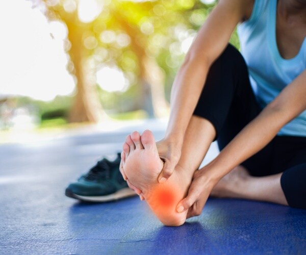 woman sitting on mat holding underneath of foot highlighted in red because painful