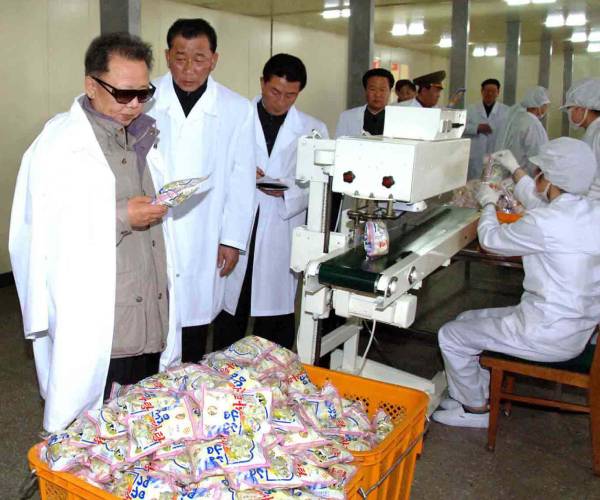 kim jong ill looks at a package of food from a bin as a worker is seen in the background