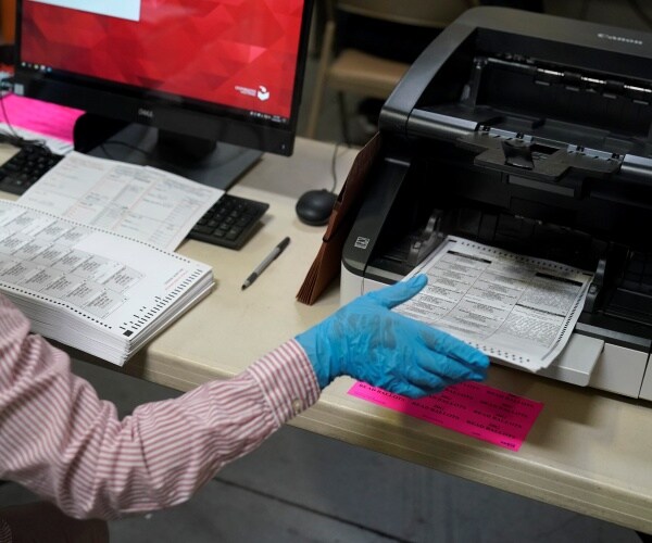 worker loads mail in ballots into machine