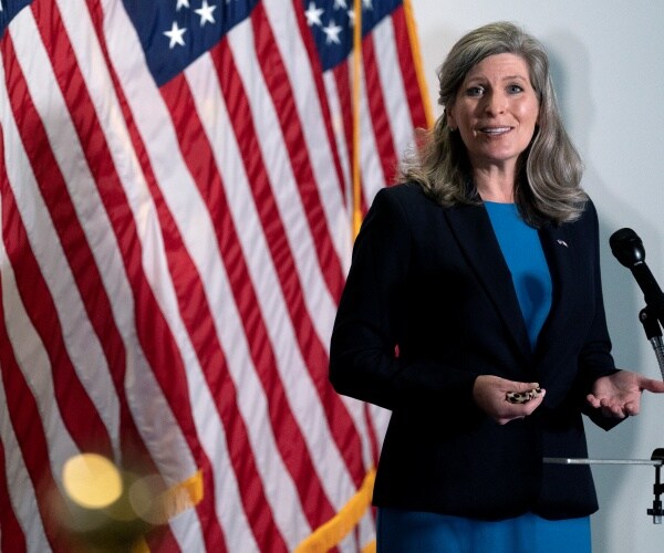 joni ernst stands in front of flags