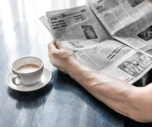 man reading newspaper in the morning with a cup of coffee
