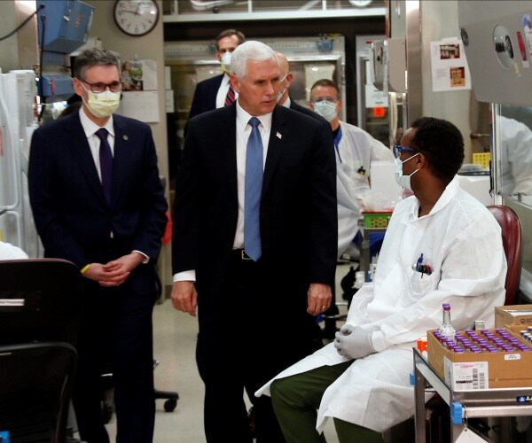 mike pence in a suit talks to a researcher and other clinic workers in white labcoats