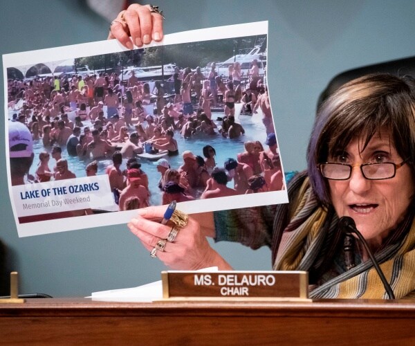 delauro speaks into a mic while holding a picture of people partying in the lake of the ozarks