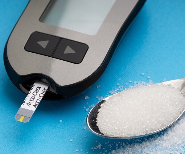 glucose meter next to spoonful of sugar