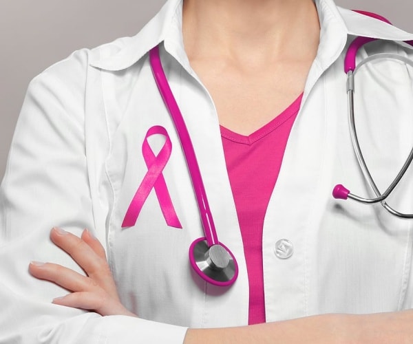 doctor in white coat, pink t-shirt, stethoscope, pink ribbon on coat for breast cancer