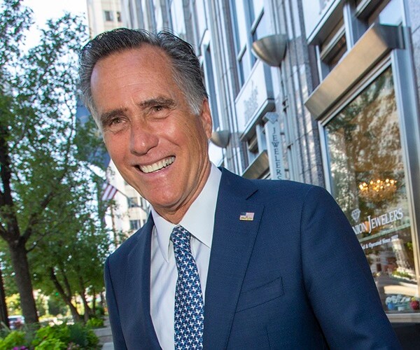 mitt romney walks across a sidewalk in salt lake city