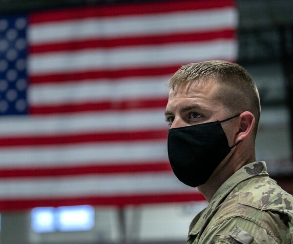 soldier wearing mask stands in front of american flag