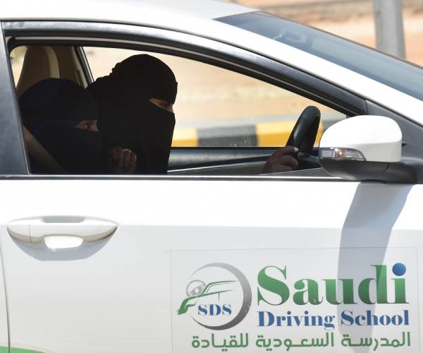 two women wearing head coverings in a car reading saudi driving school