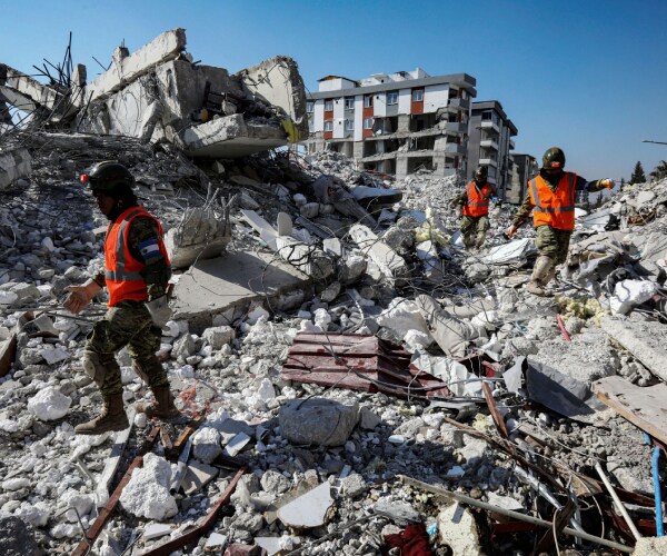 three workers walking through building rubble