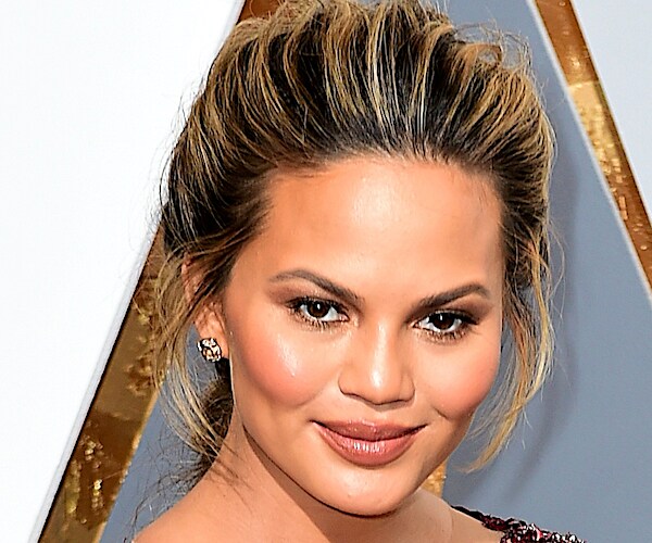 chrissy teigen looks down and smiles on the red carpet