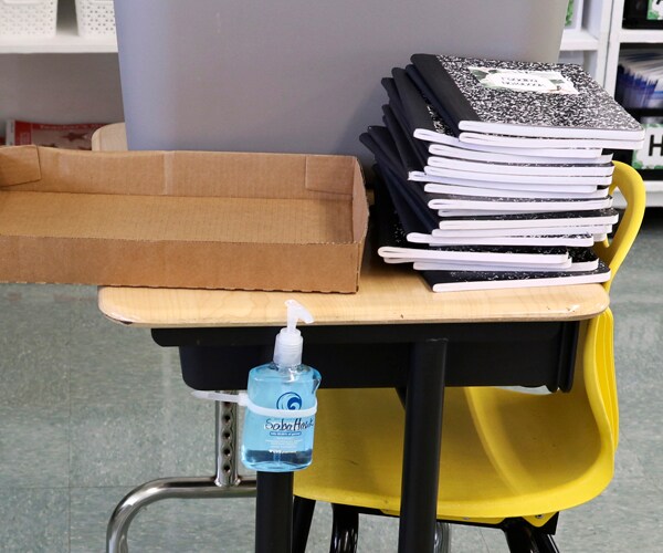 notebooks stacked up on a classroom desk with hand sanitizer attached to the side