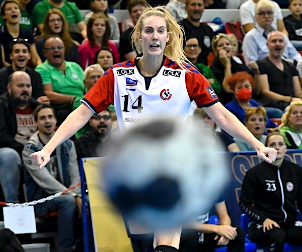 a woman playing handball has her midsection covered by a blurred out handball coming toward the camera lens