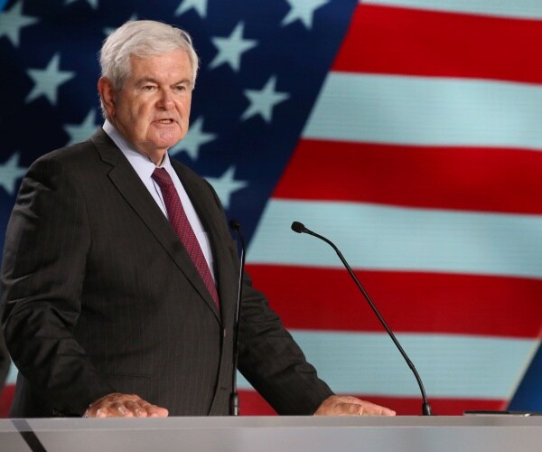 newt gingrich in a suit and purple tie standing in front of a projected american flag