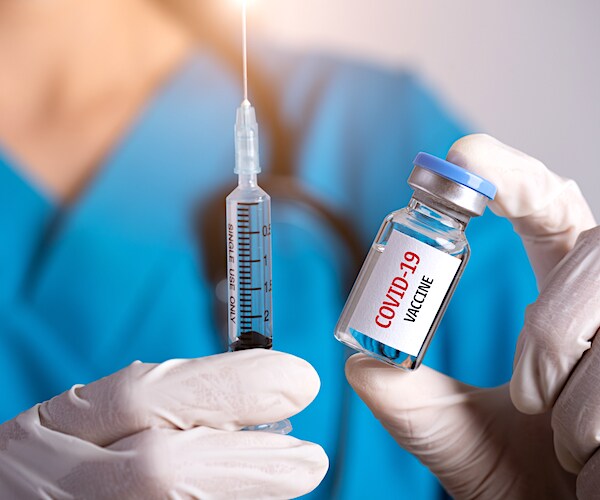 a photo illustration of a nurse holding a syringe, needle, and a vile marks covid-19 vaccine