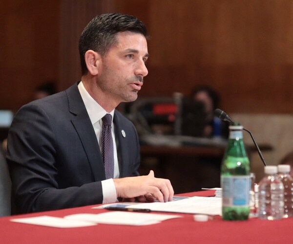 chad wolf in a dark gray suit and patterned tie speaking at a hearing