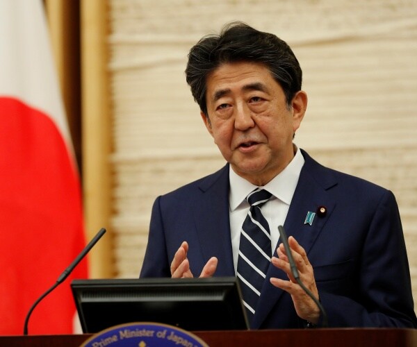 abe in a suit and striped tie standing next to a japanese flag