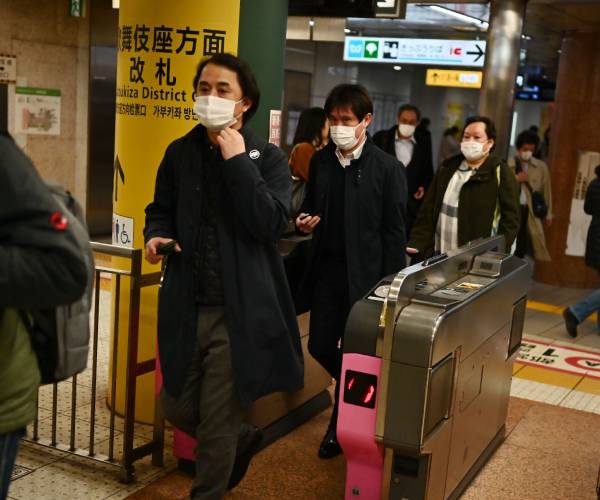 people walk through a turnstile wearing masks in Japan