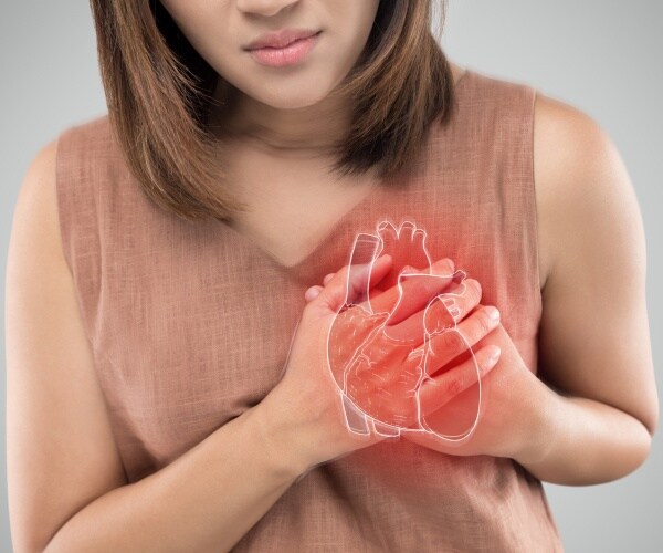 woman in a tan top holding her chest with a heart drawing overlay
