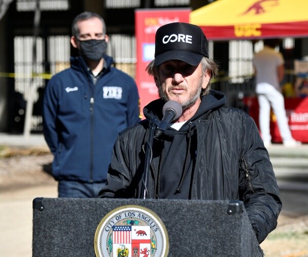 sean penn wears a core hat and stands at a lectern speaking