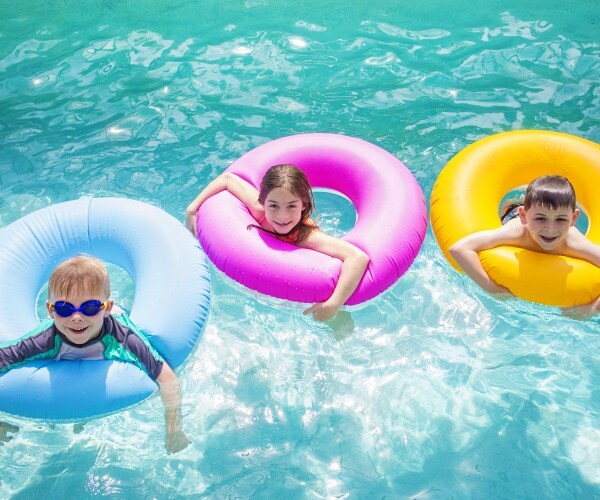 three kids smiling while floating in tubes in a pool