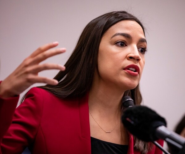 aoc in a red blazer and black top speaking into a mic
