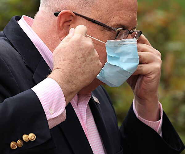 larry hogan puts a facemask on his face before a news conference