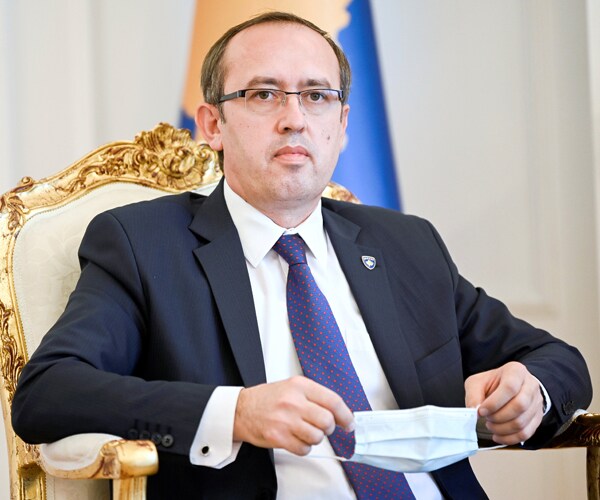 kosovo prime minister avdullah hoti sitting in a chair and holding a medical face mask