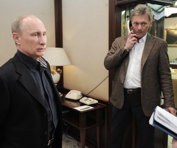 putin in a black coat and peskov in a brown blazer and white shirt
