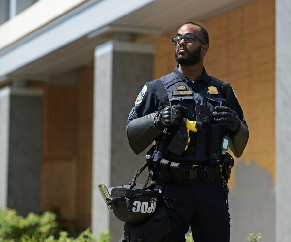 police officer in a uniform carrying his helmet clipped to his utility belt
