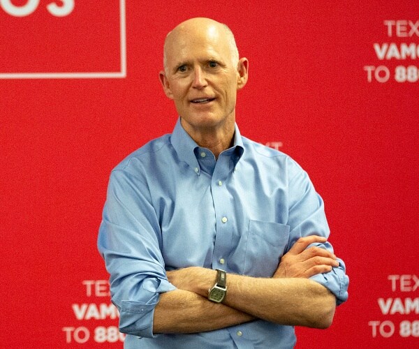 rick scott stands in front of banner wall
