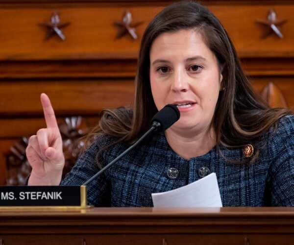 stefanik in a blue and black plaid coat speaking at a hearing