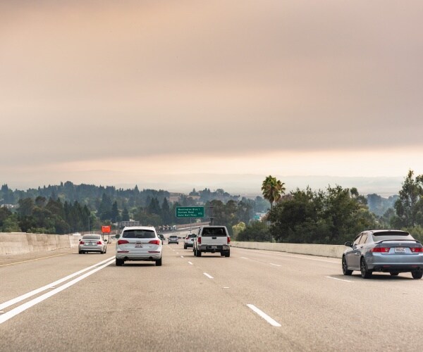 cars on freeway with smoke clouds in distance due to wildfires 