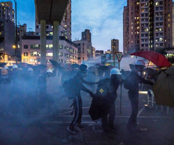 protestors with umbrellas, hardhats and facemasks try to avoid tear gas