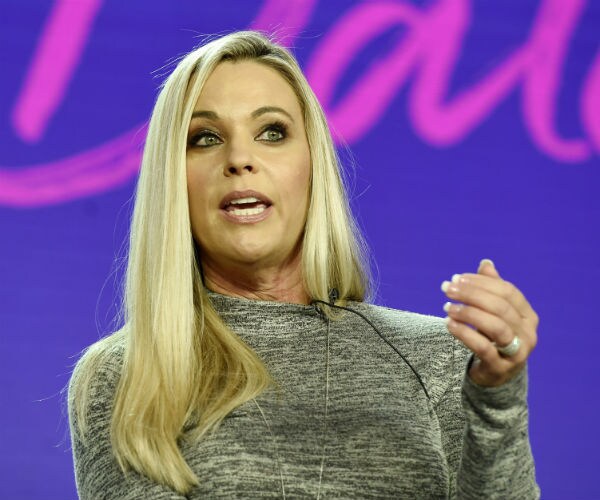 Kate Gosselin is shortn in a gray dress doing an interview. 