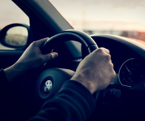 man driving a bmw with both hands on steering wheel