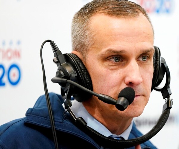 corey lewandowski wears a headset and a team trump jacket