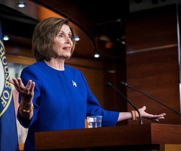 pelosi in a cobalt blue suit speaking at a podium